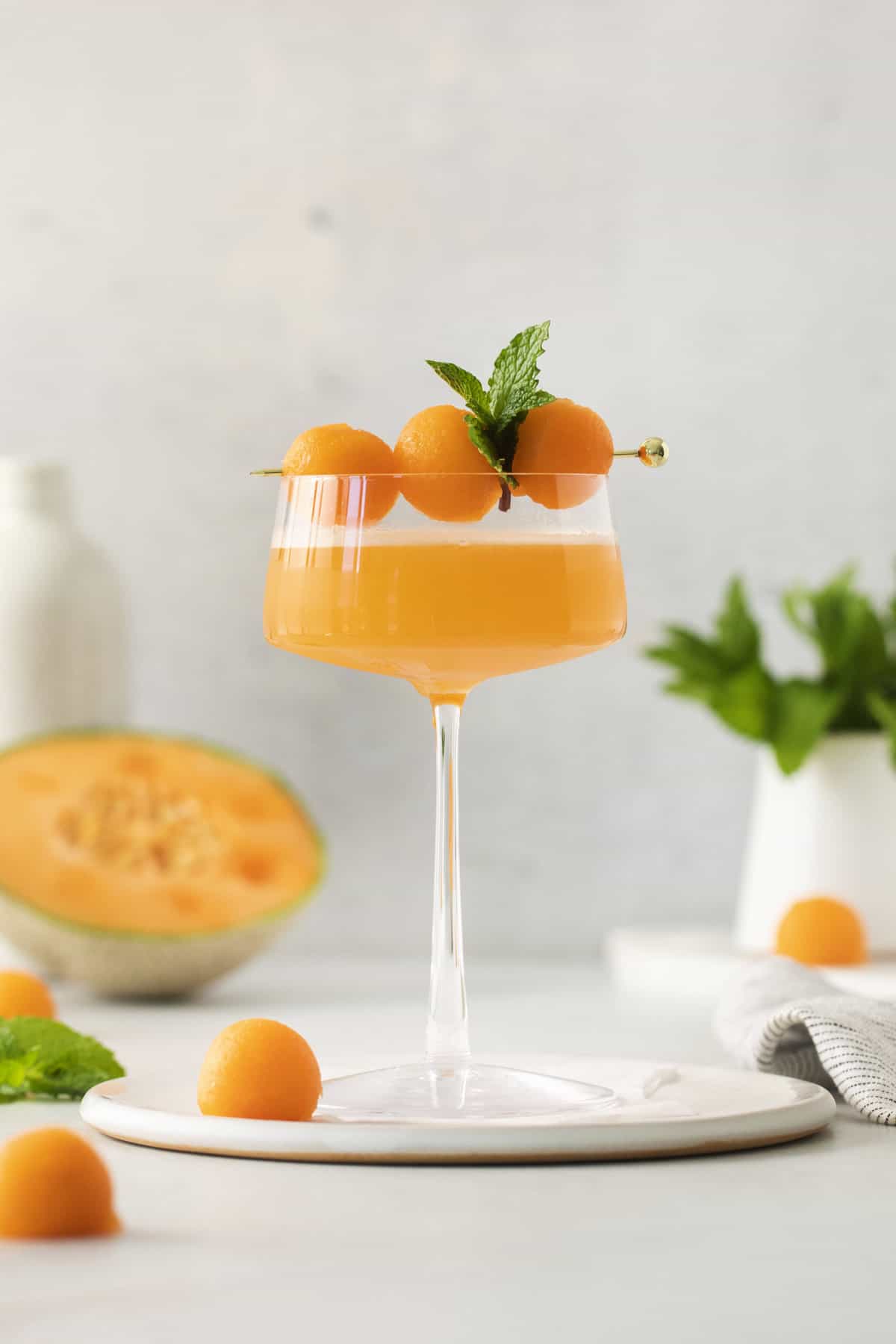 side view of a glass with a cantaloupe ginger cocktail garnished with melon balls and mint.