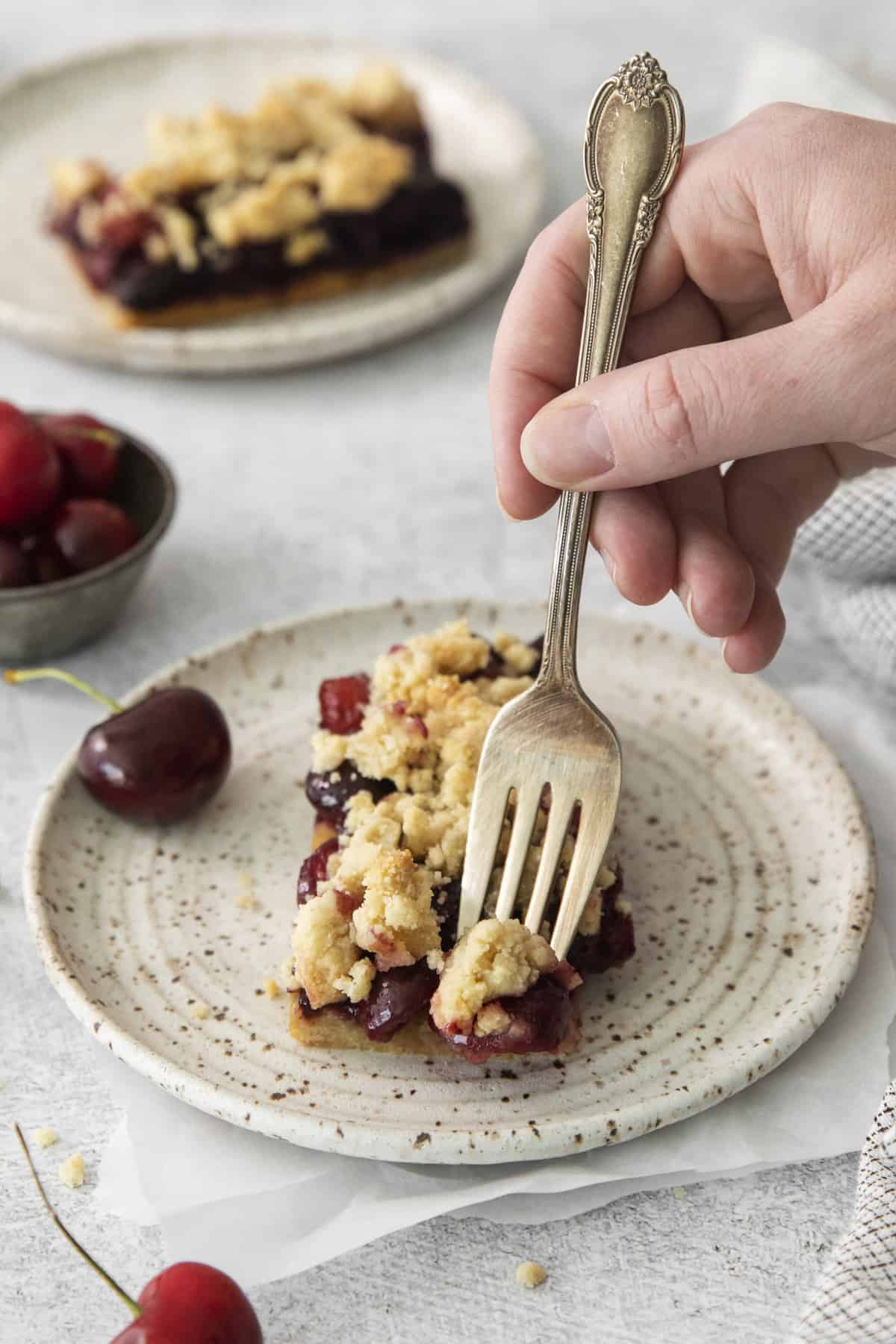 a fork being plunged into a cherry pie bar on a plate.