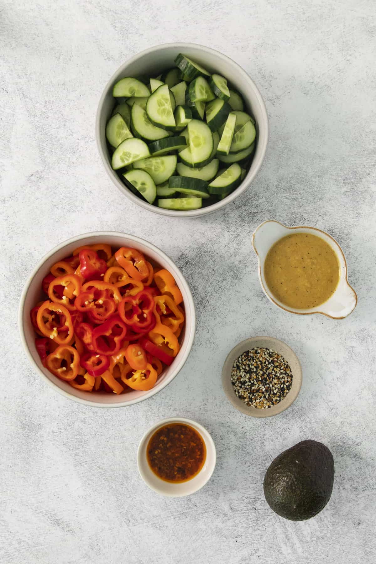 overhead of cucumber pepper salad ingredients in separate bowls.