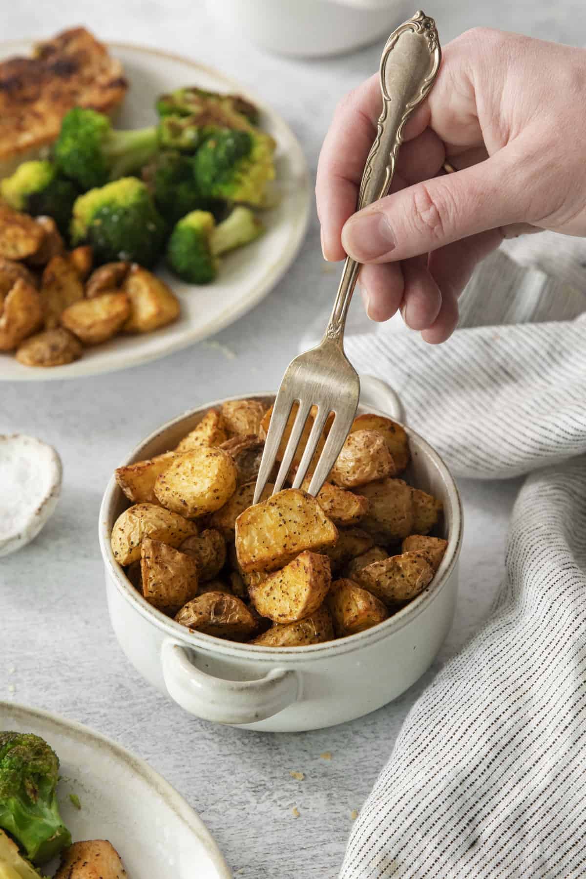 a fork being used to pick a roasted potato chunk out of a bowl.