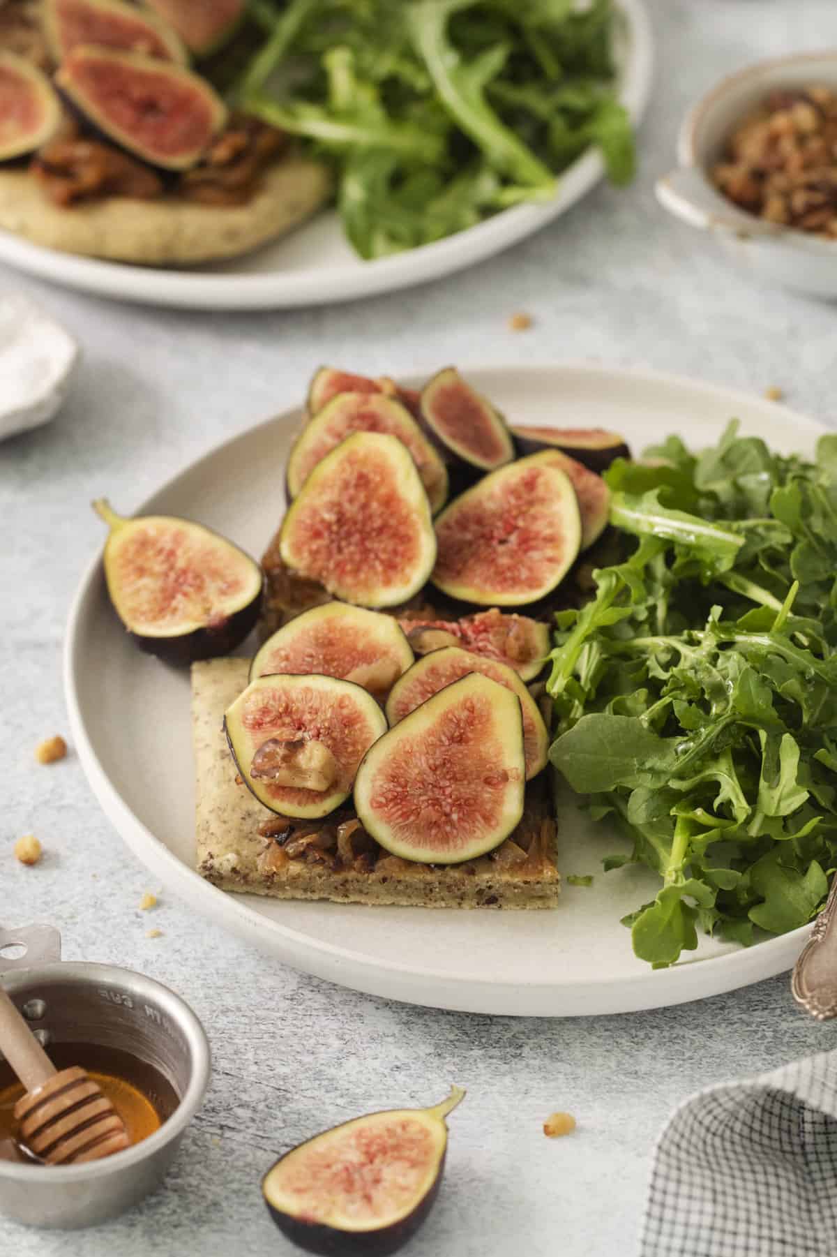 a piece of fig pizza on a plate with a side salad.