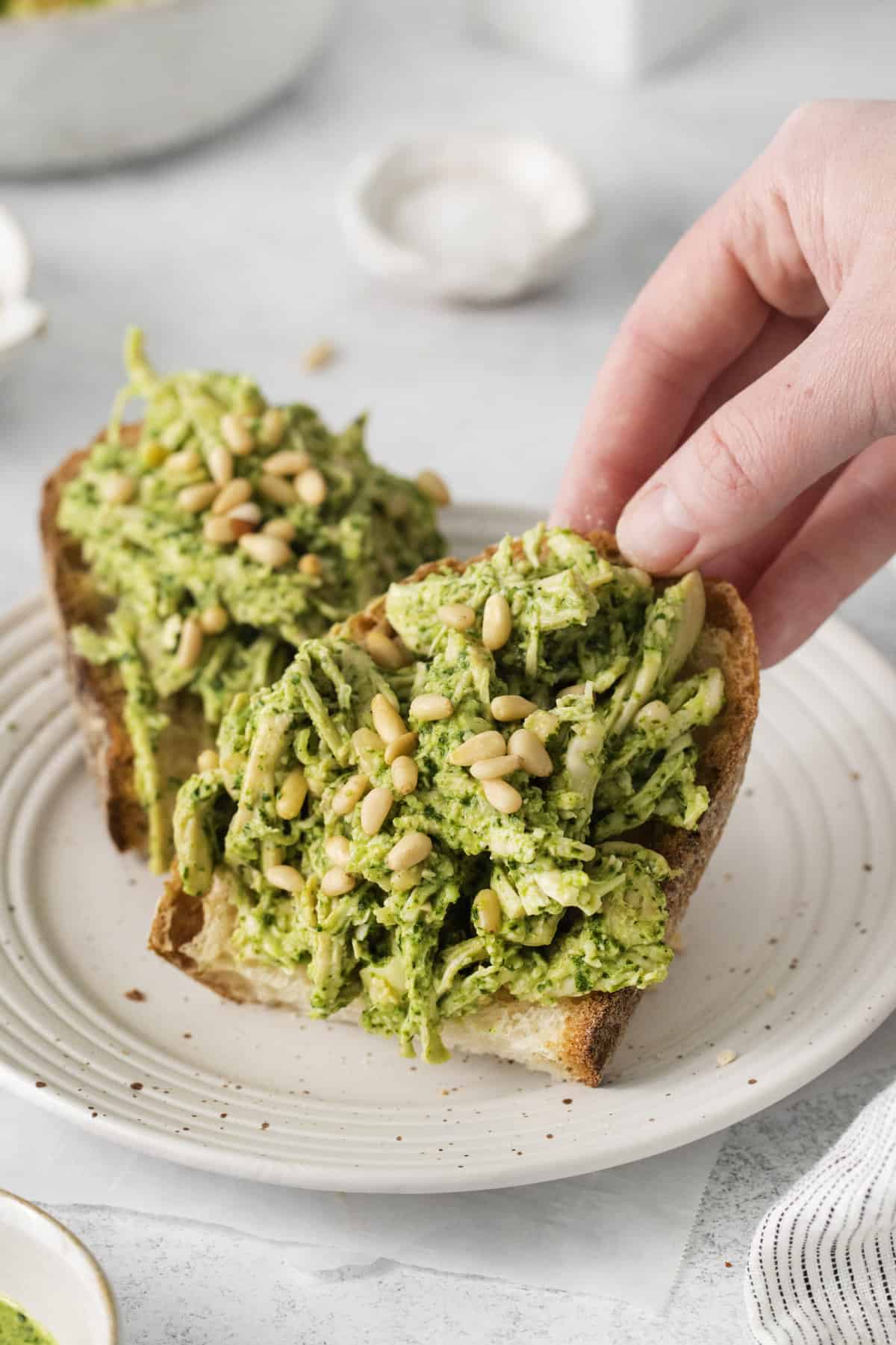 half of a piece of toast topped with pesto chicken salad being lifted off of a plate.