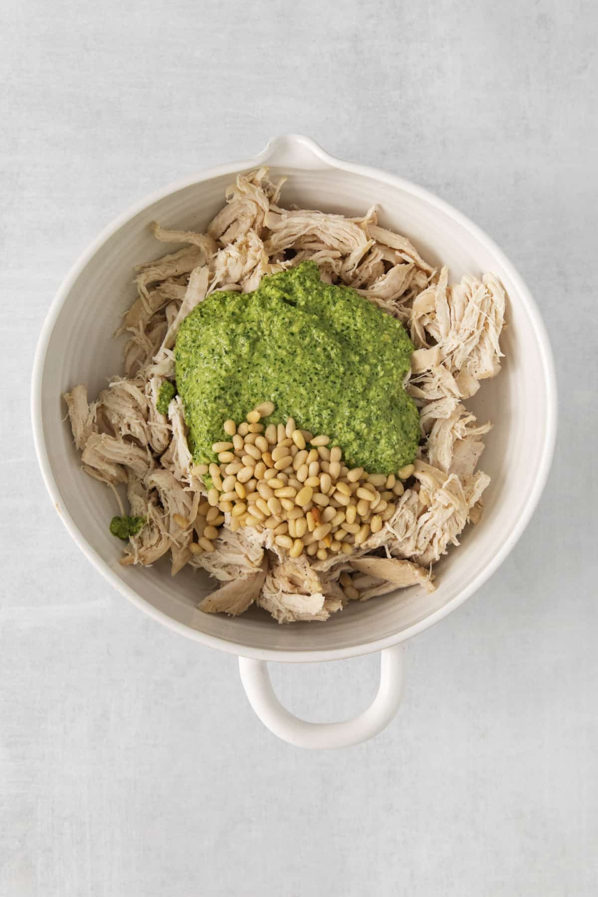 chicken, pesto, and pine nuts in a mixing bowl.