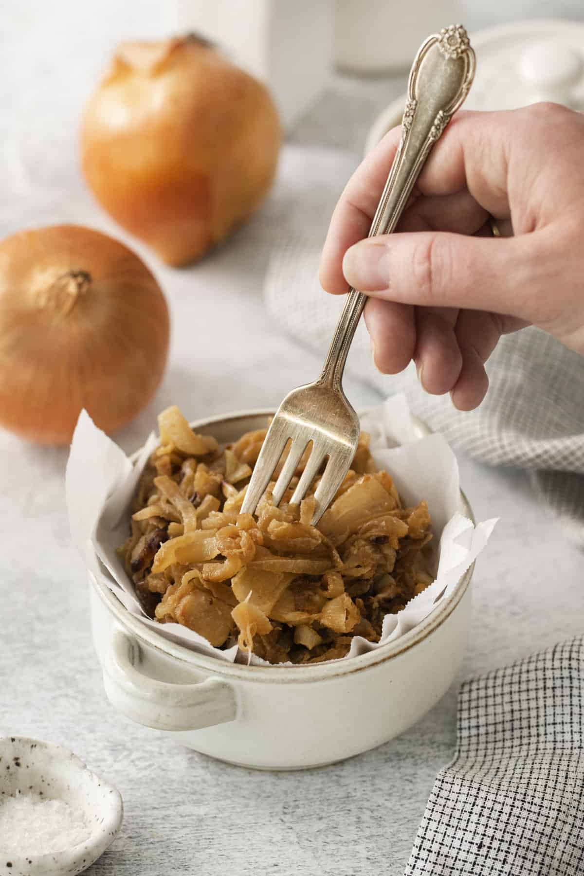 a fork being plunged into a bowl filled with caramelized onions.