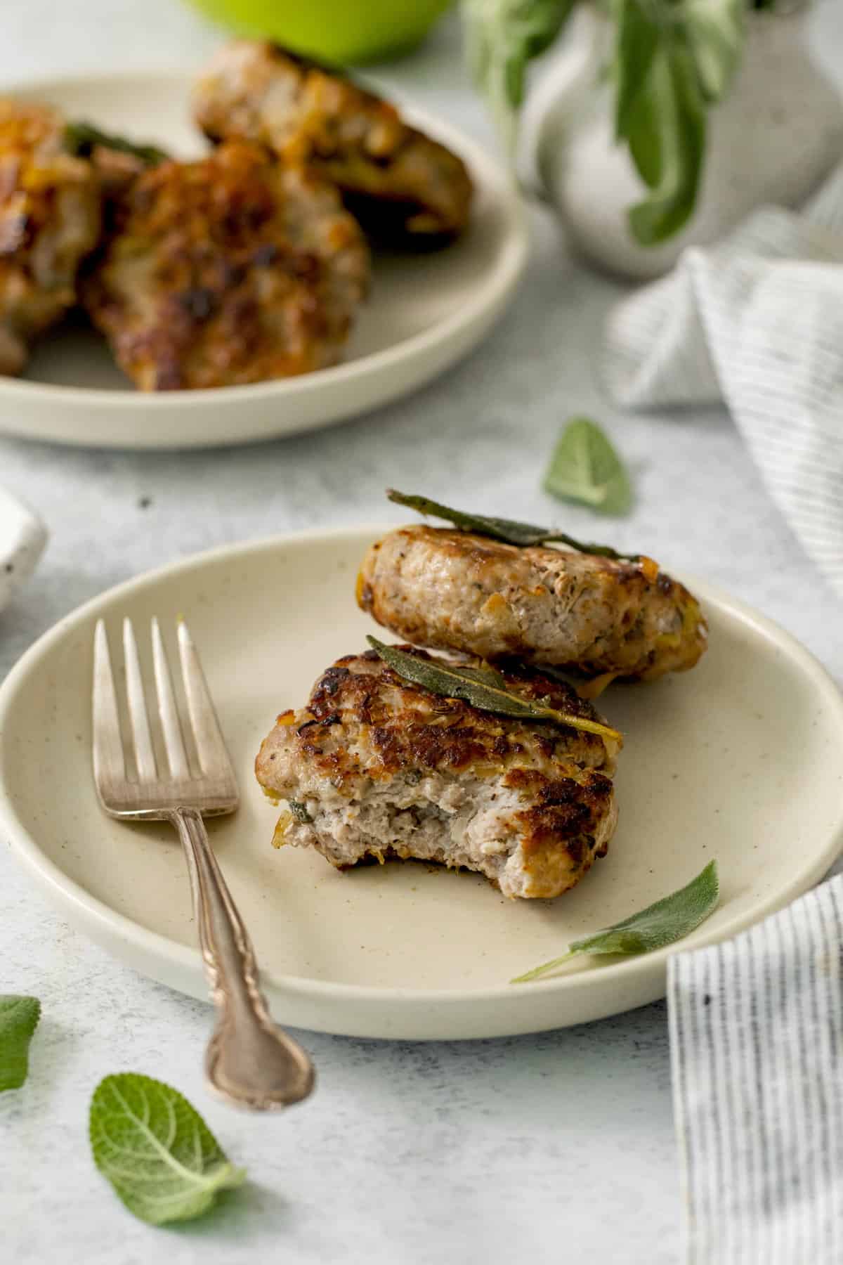 two breakfast sausage patties on a plate, one with a bite taken out.