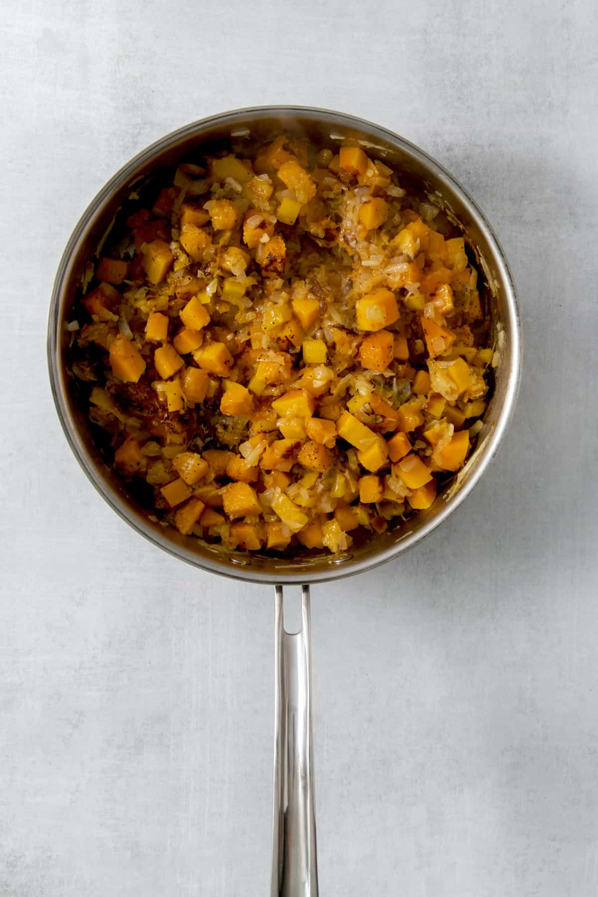 cooked potatoes, squash, onion, and pepper in a pan.
