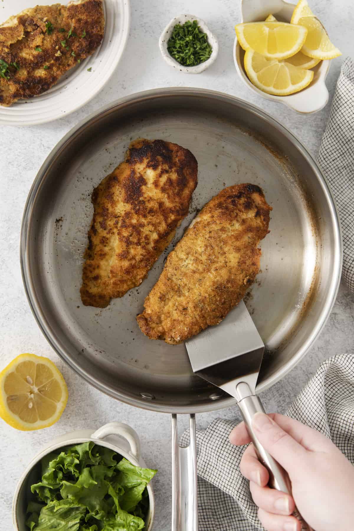 two chicken cutlets in a pan, one being lifted with a spatula.
