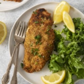 a plate with a paleo chicken cutlet next to a salad and lemon.