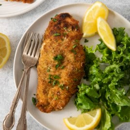 a plate with a paleo chicken cutlet next to a salad and lemon.