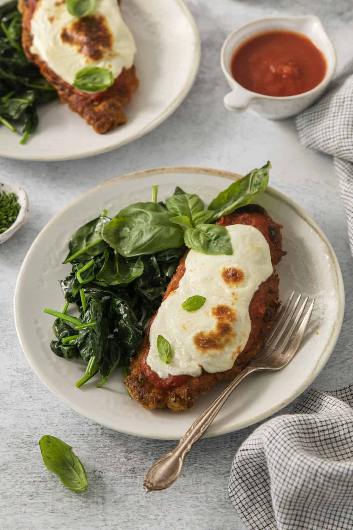 a plate filled with chicken parm, greens, and fresh basil.