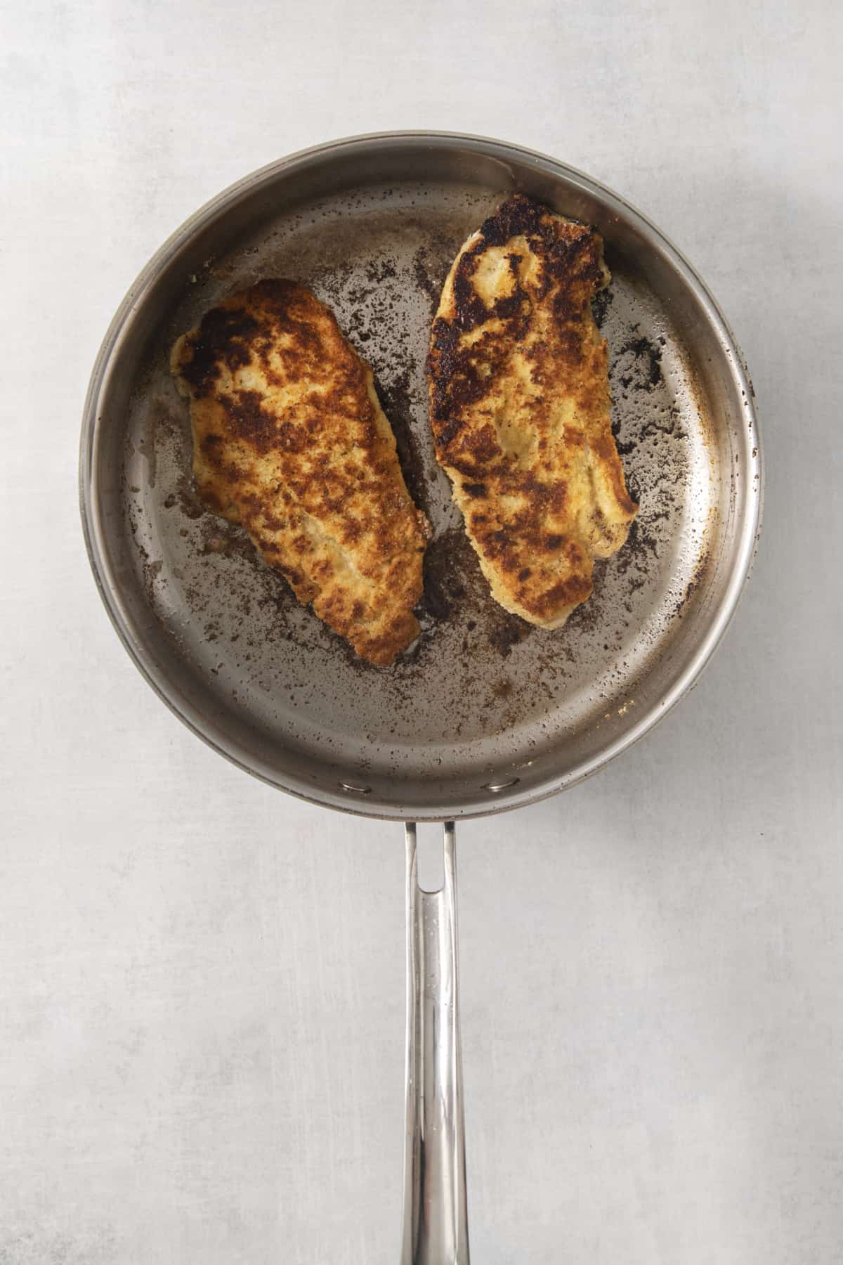 chicken cutlets being pan fried in a skillet.