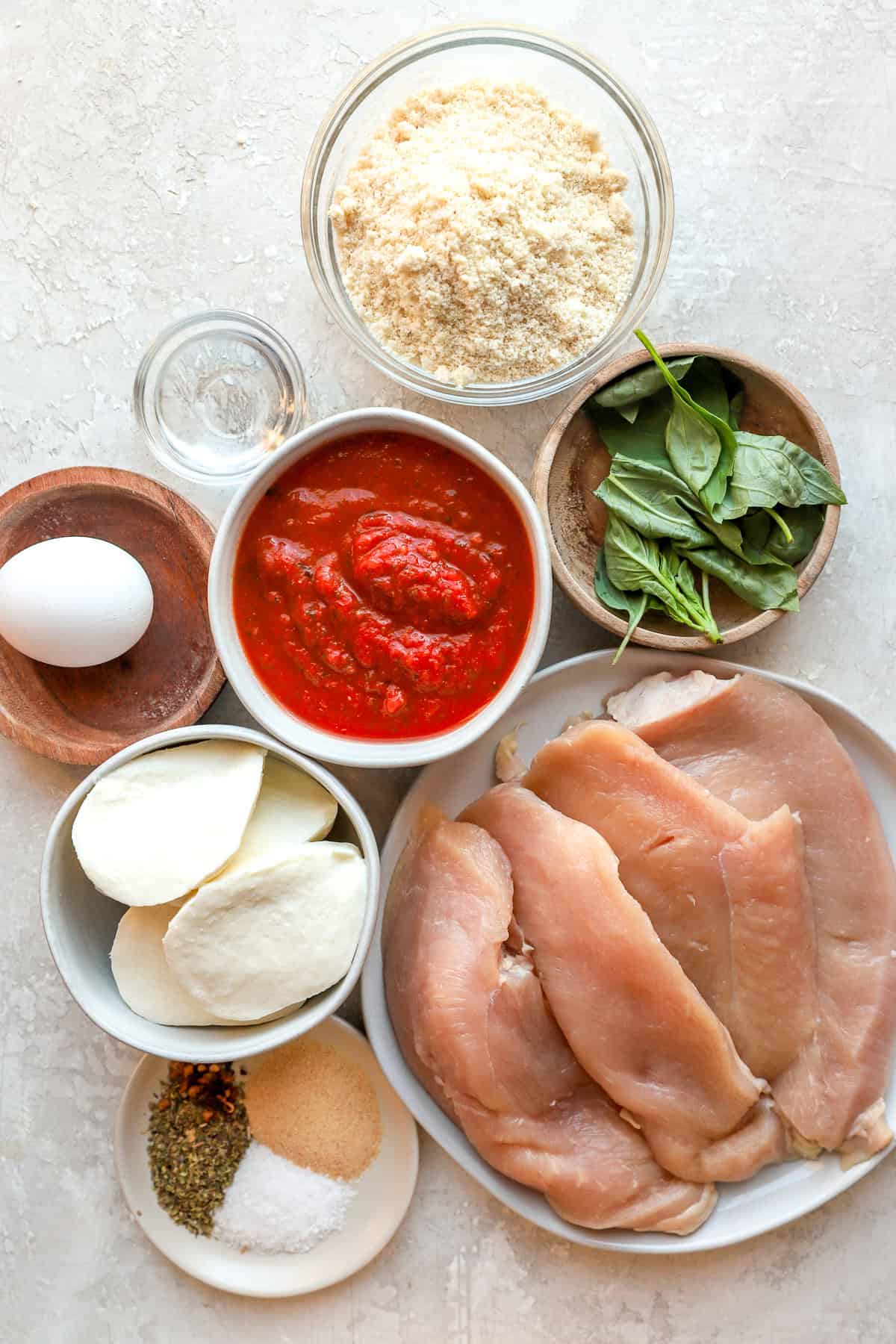 All ingredients laid out in bowls: egg, spinach, bread crumbs, seasonings, marinara sauce, mozzarella, chicken.