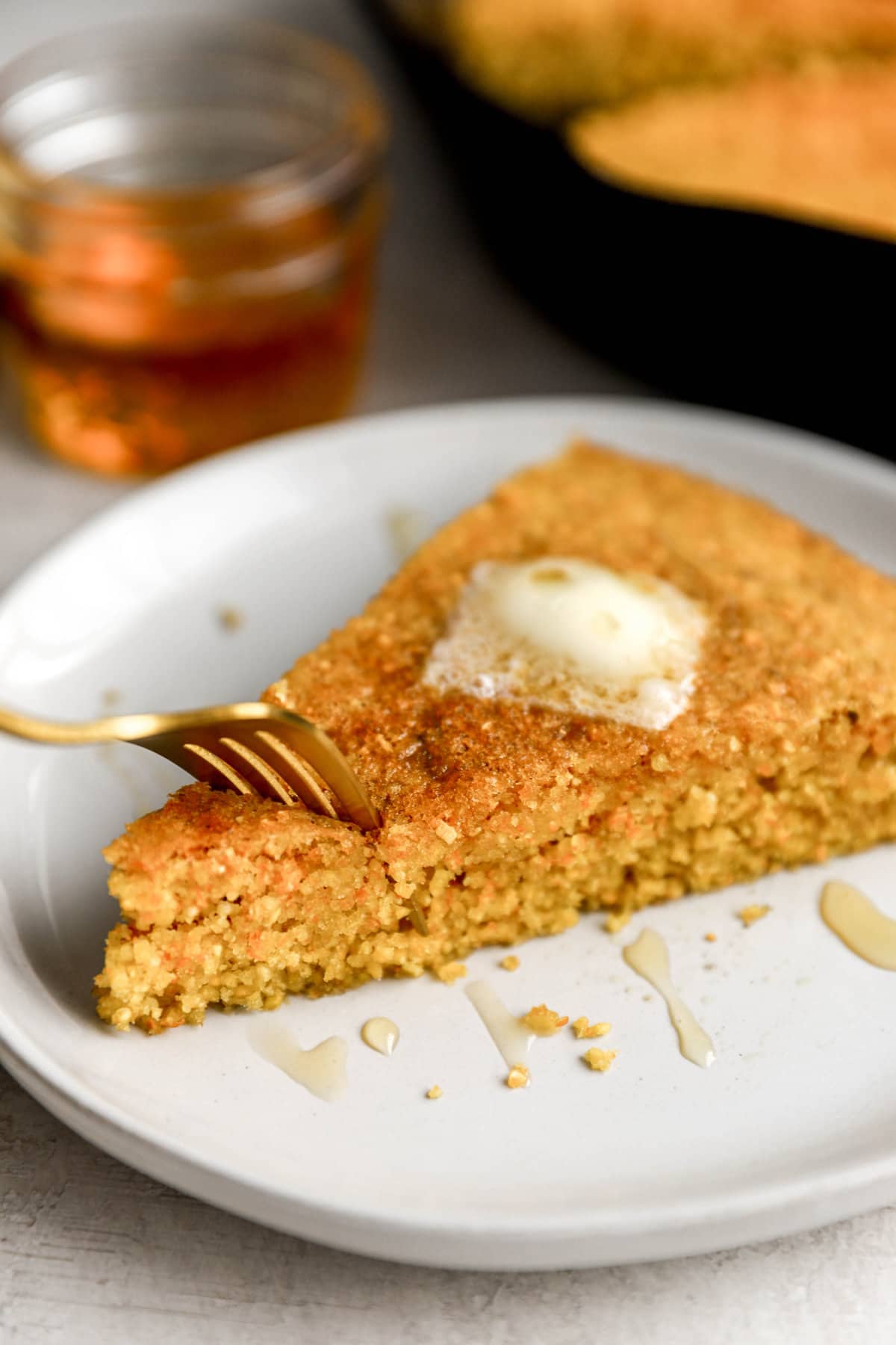 a fork being plunged into a slice of cornbread topped with butter.