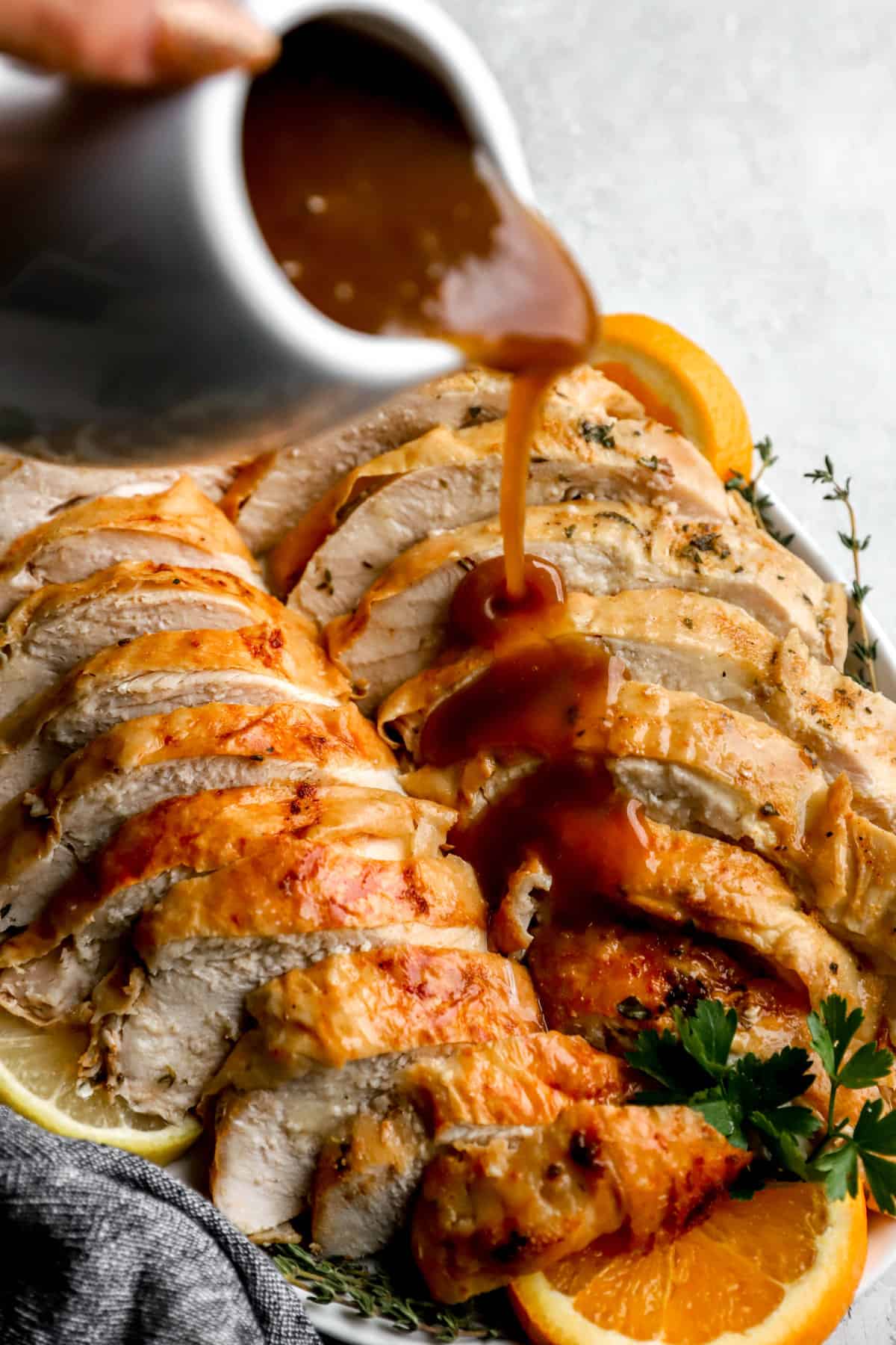 turkey gravy from drippings being drizzled over a roast turkey on a platter.