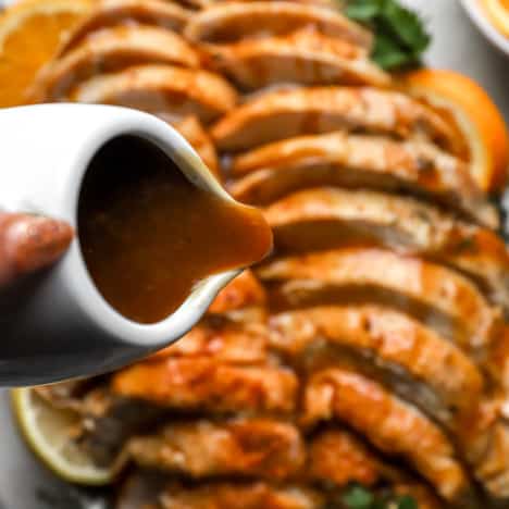a small pitcher of turkey gravy being poured over a sliced roast turkey.