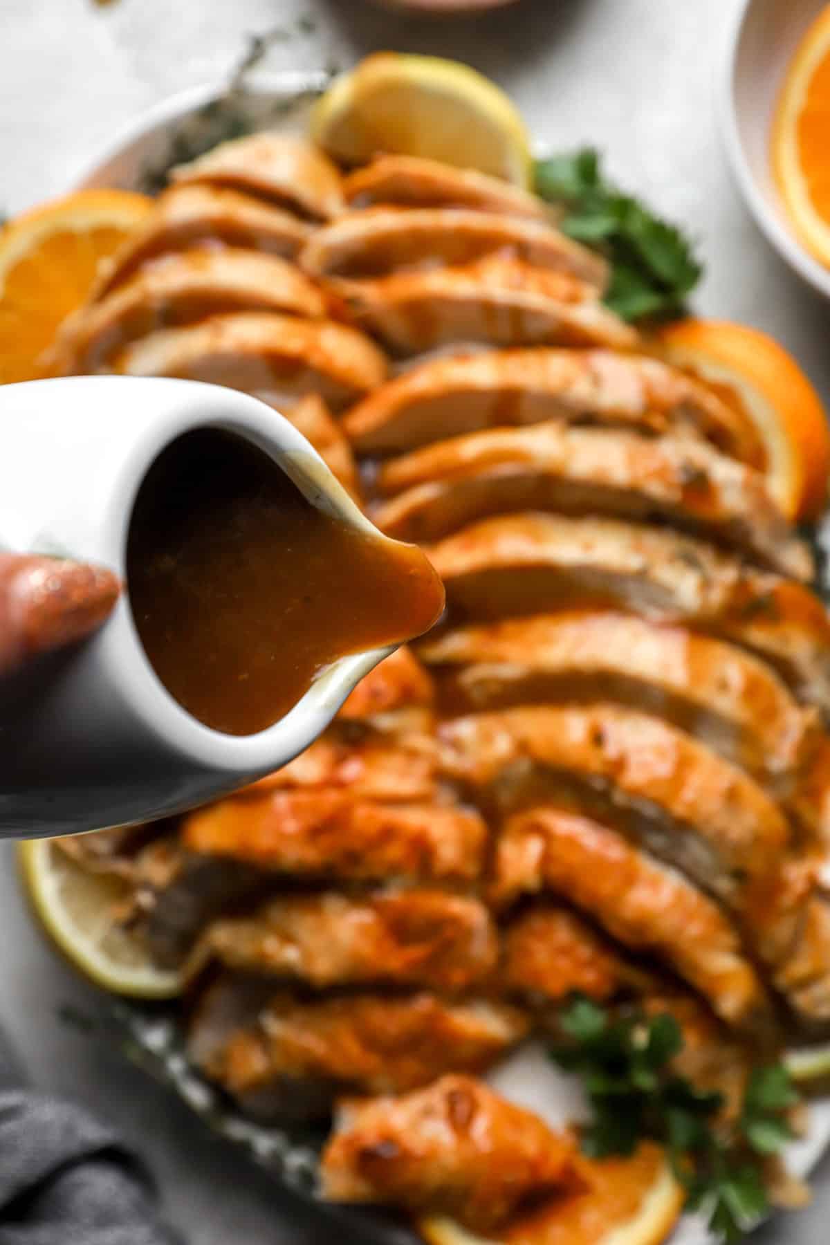 a small pitcher of turkey gravy being poured over a sliced roast turkey.