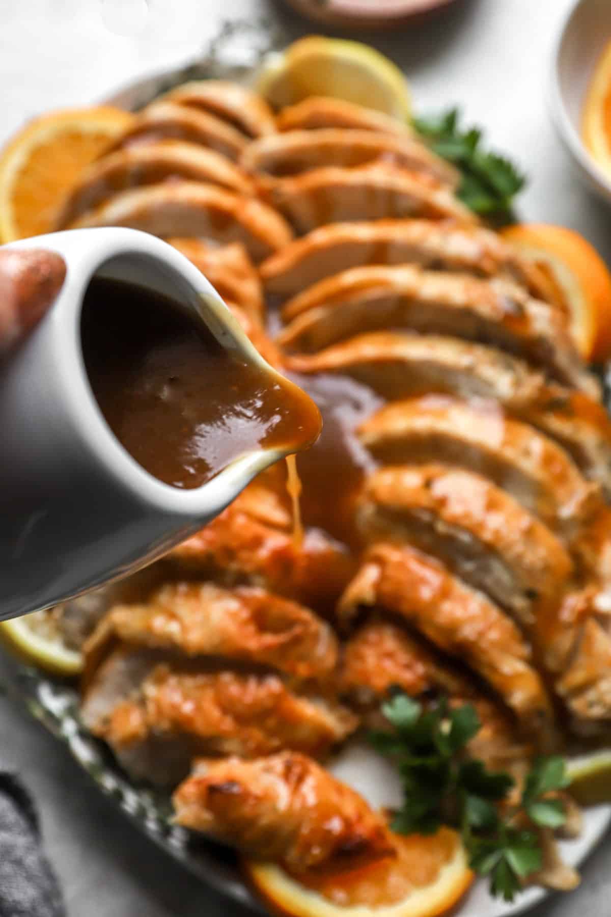 a small pitcher of turkey gravy being poured over a sliced roast turkey.