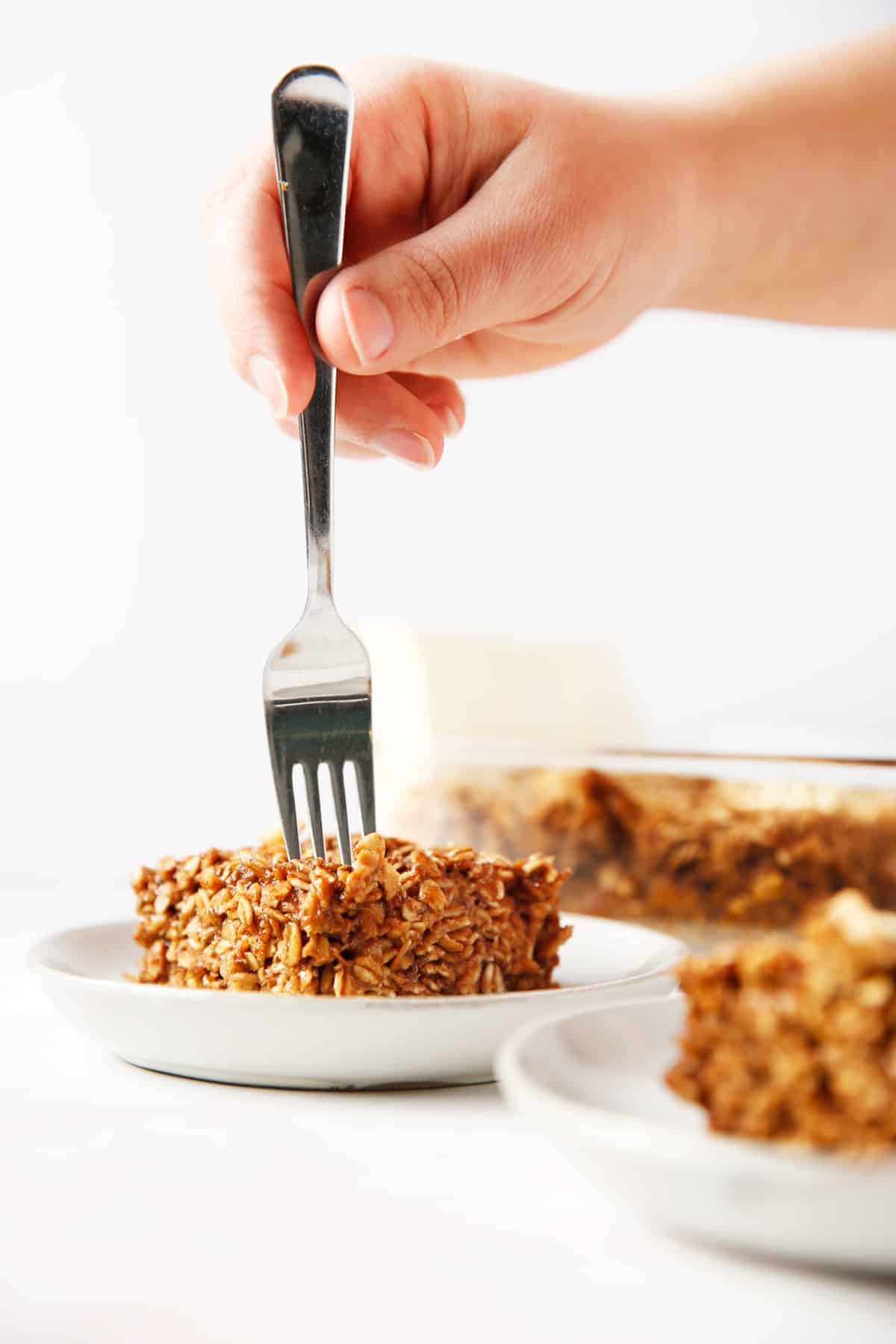 a hand holding a fork and placing into a place of baked gingerbread oatmeal.
