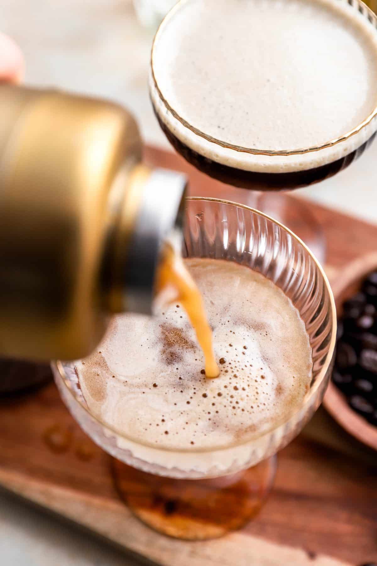 an espresso martini being poured out of a shaker into a glass from above.