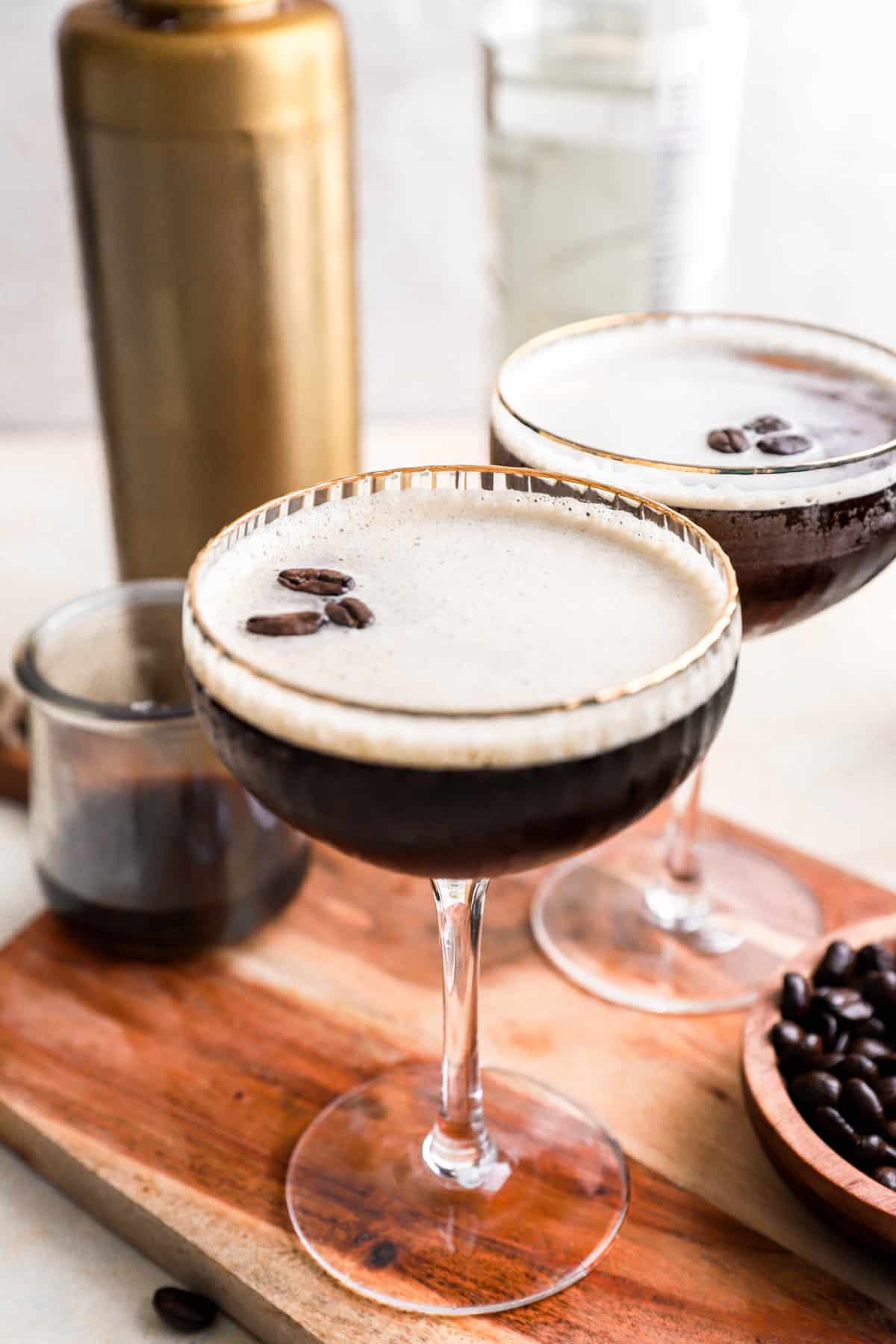 slight overhead of two espresso martinis in front of a cocktail shaker.