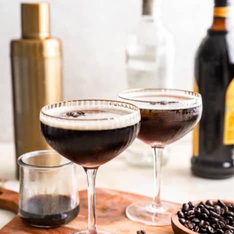two glasses filled with espresso martinis with bottles of liqueur in the background.