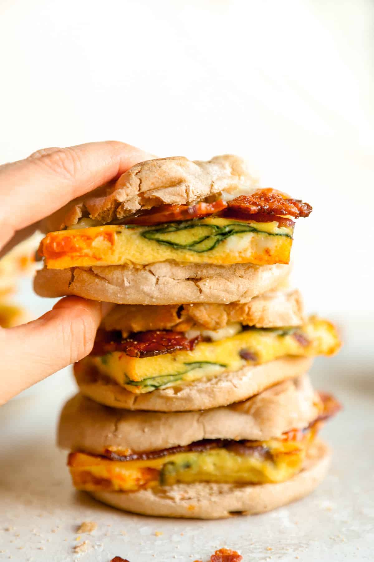one breakfast egg sandwich being lifted off a pile of three.
