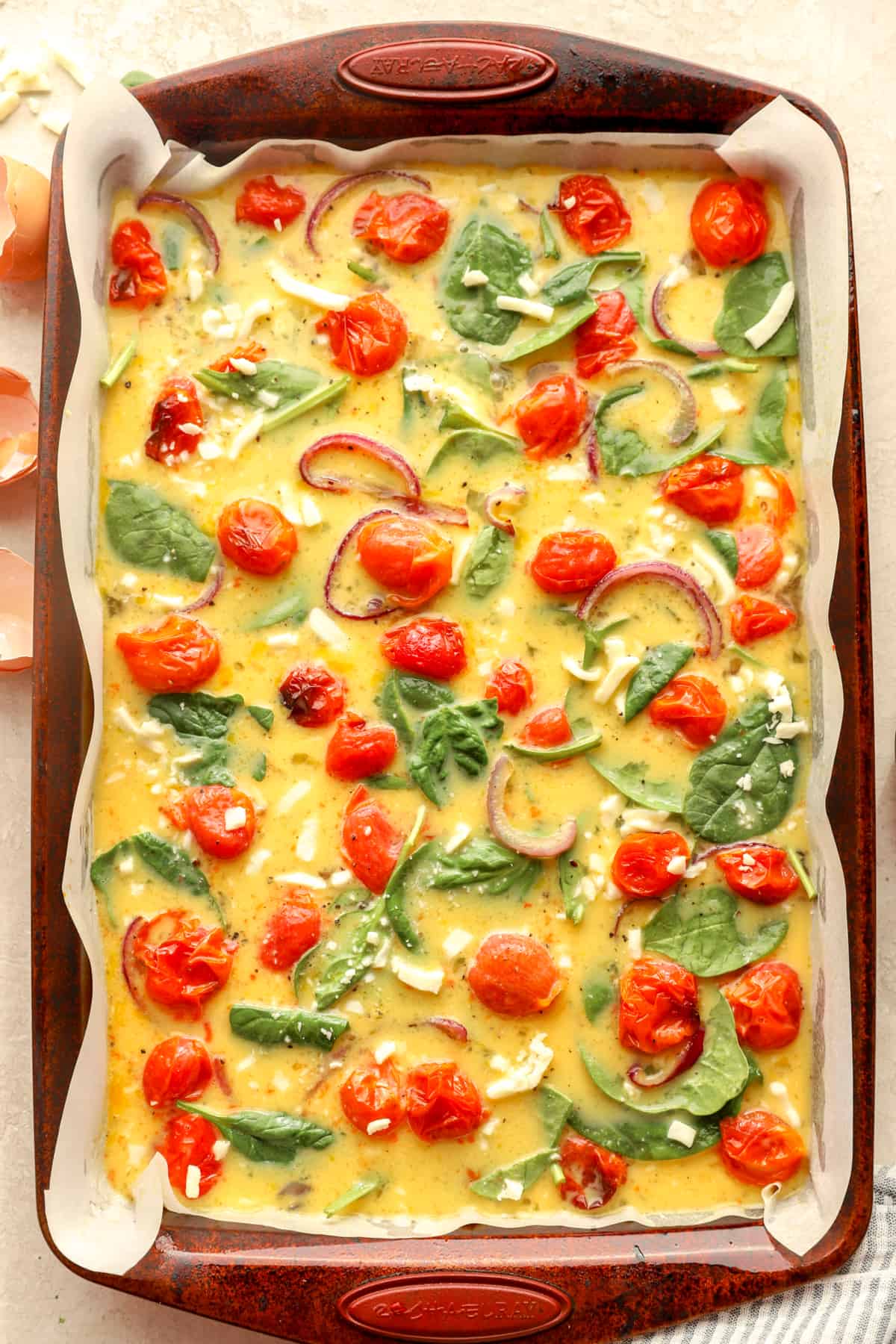 egg with spinach and tomato unbaked in a sheet pan.
