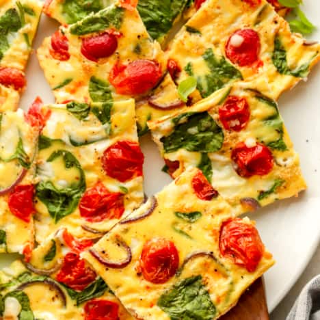 above image of square slices of egg frittata with spinach and tomato on a serving platter.