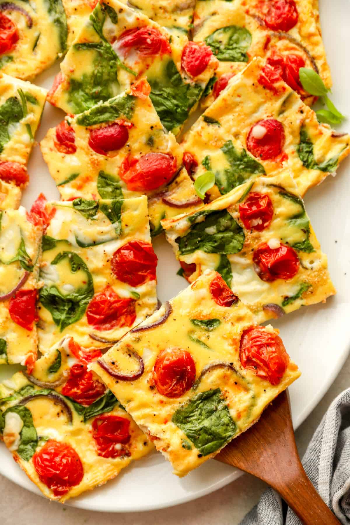 Pictured above are square egg frittata slices with spinach and tomatoes on a plate.