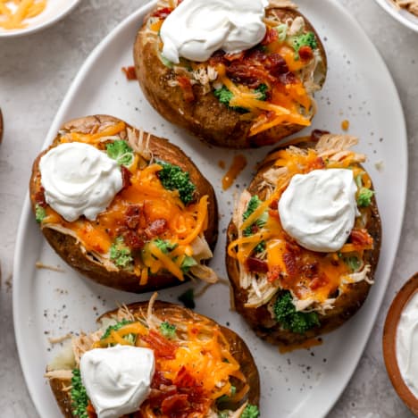 above image of air fryer baked potatoes on a plate loaded with cheese, bacon, sour cream, and chives.