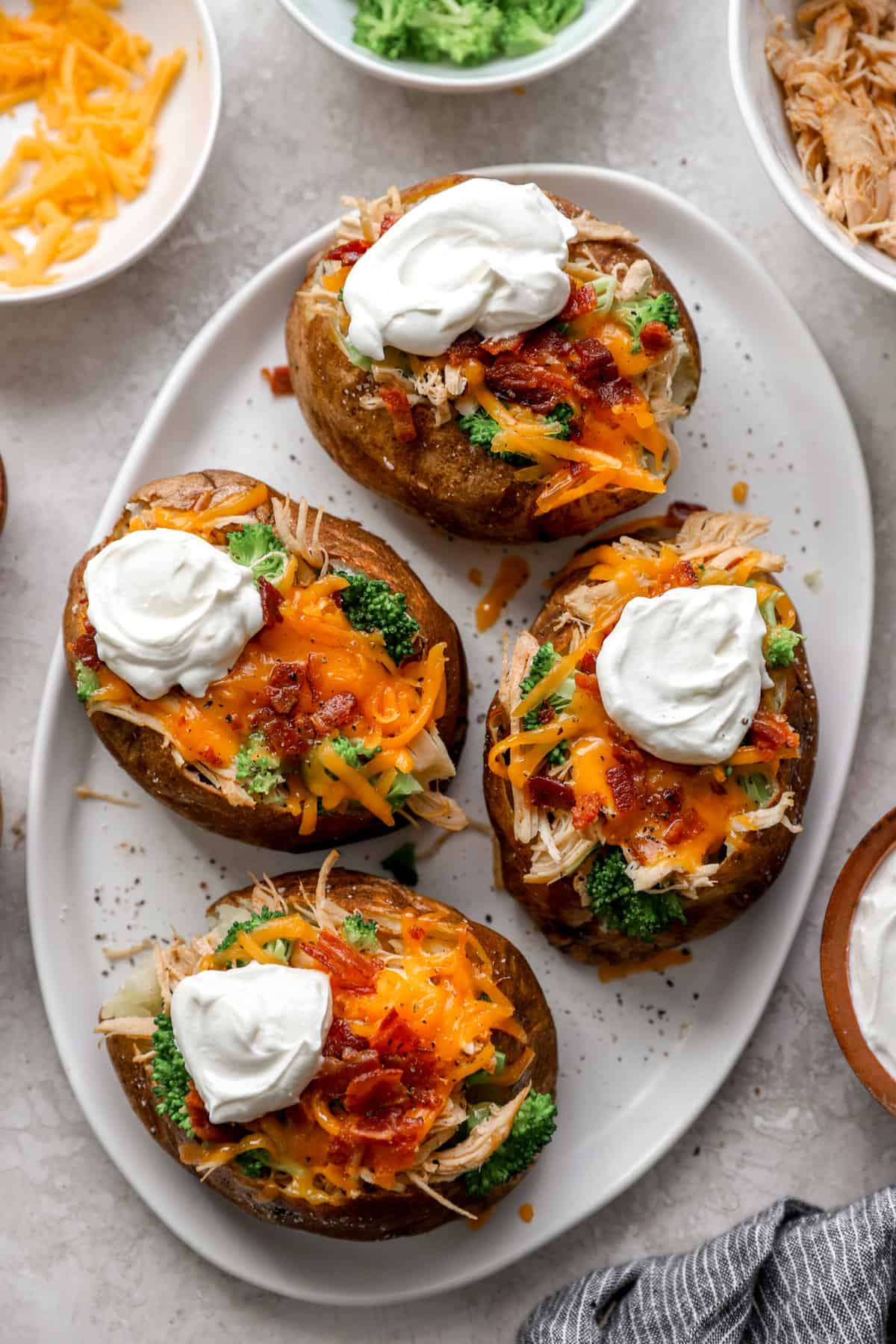 above image of air fryer baked potatoes on a plate loaded with cheese, bacon, sour cream, and chives. 