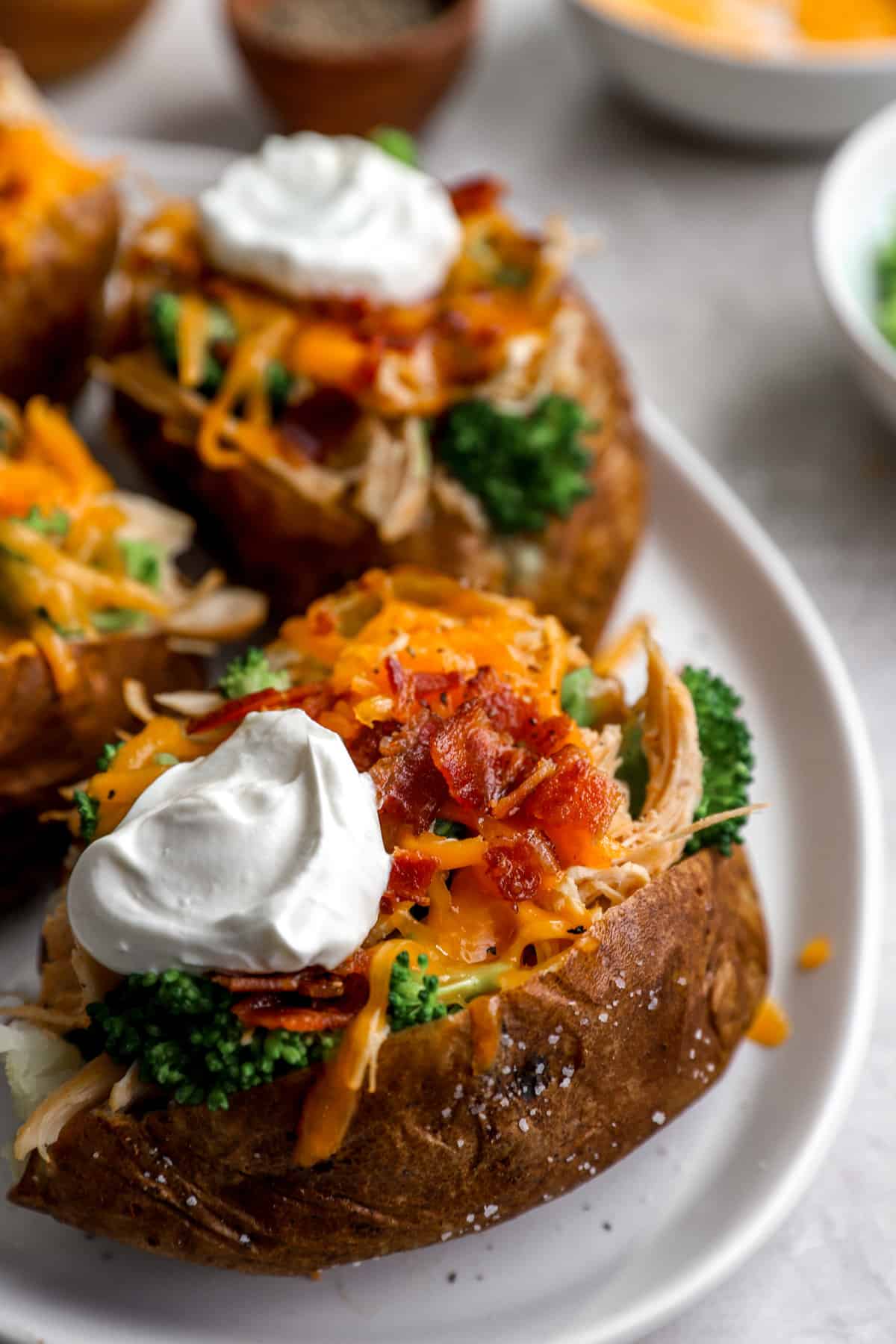 side view of air fryer baked potatoes on a plate topped with cheese, bacon, sour cream, and green onions.