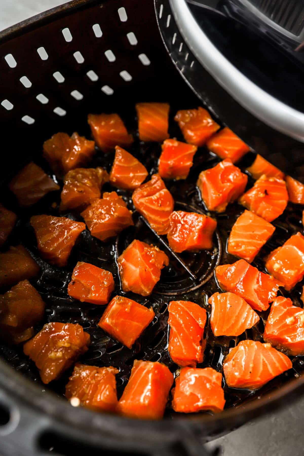 cubed salmon pieces in an air fryer basket.