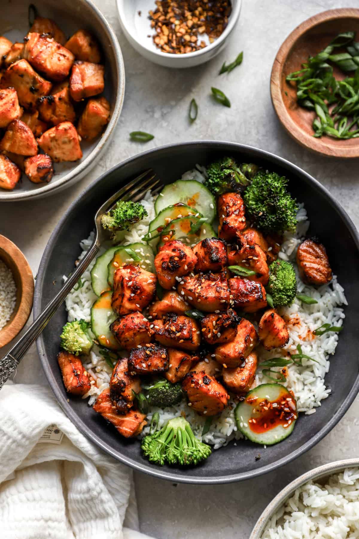 air fryer salmon pieces over a bed of rice with broccoli and cucumber.