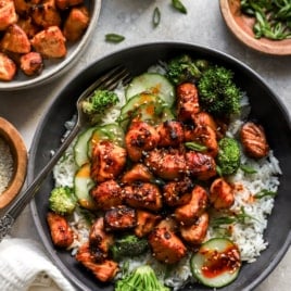 air fryer salmon pieces over a bed of rice with broccoli and cucumber.