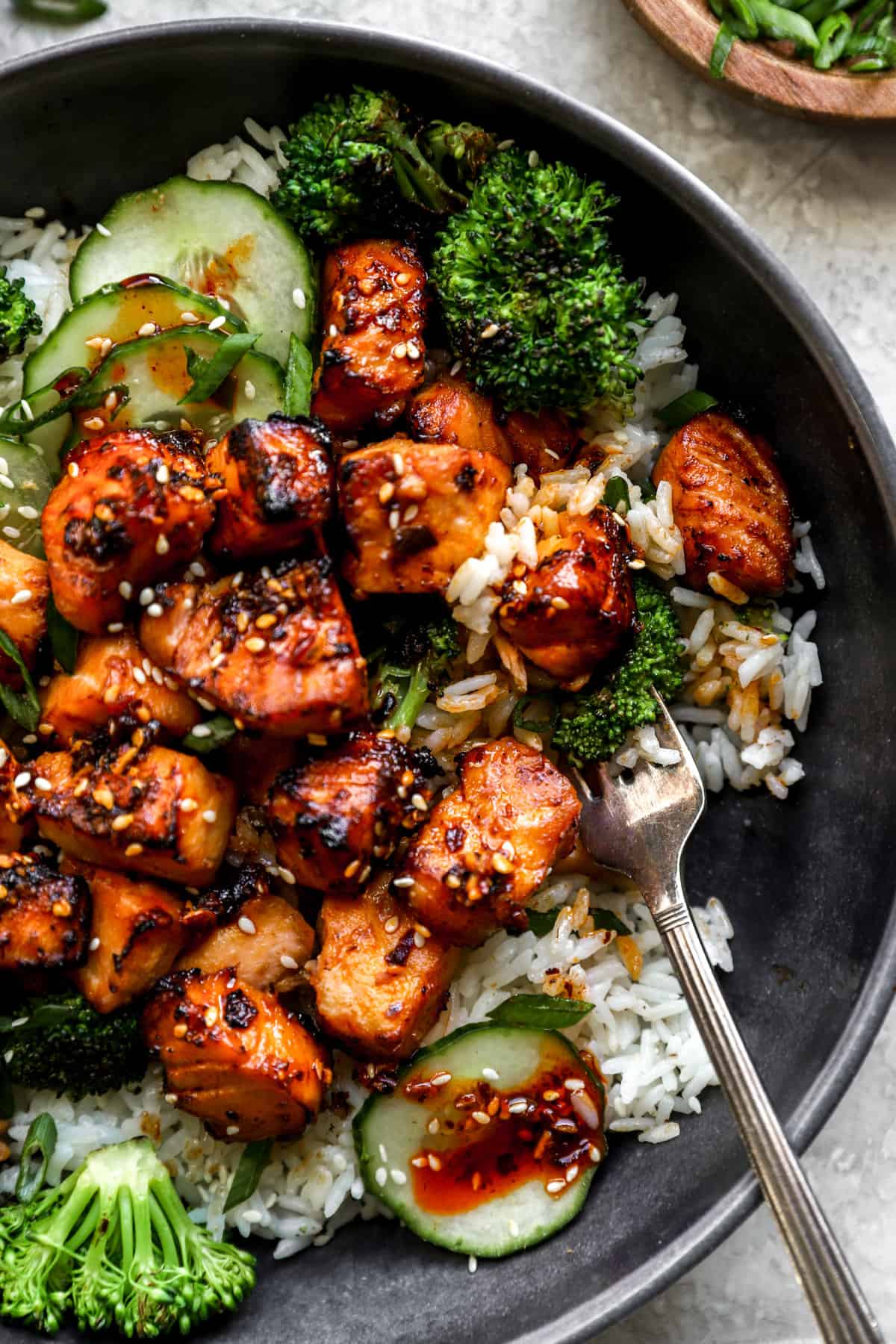 above image of air fried salmon bites on a plate over rice and topped with cucumber and broccoli.