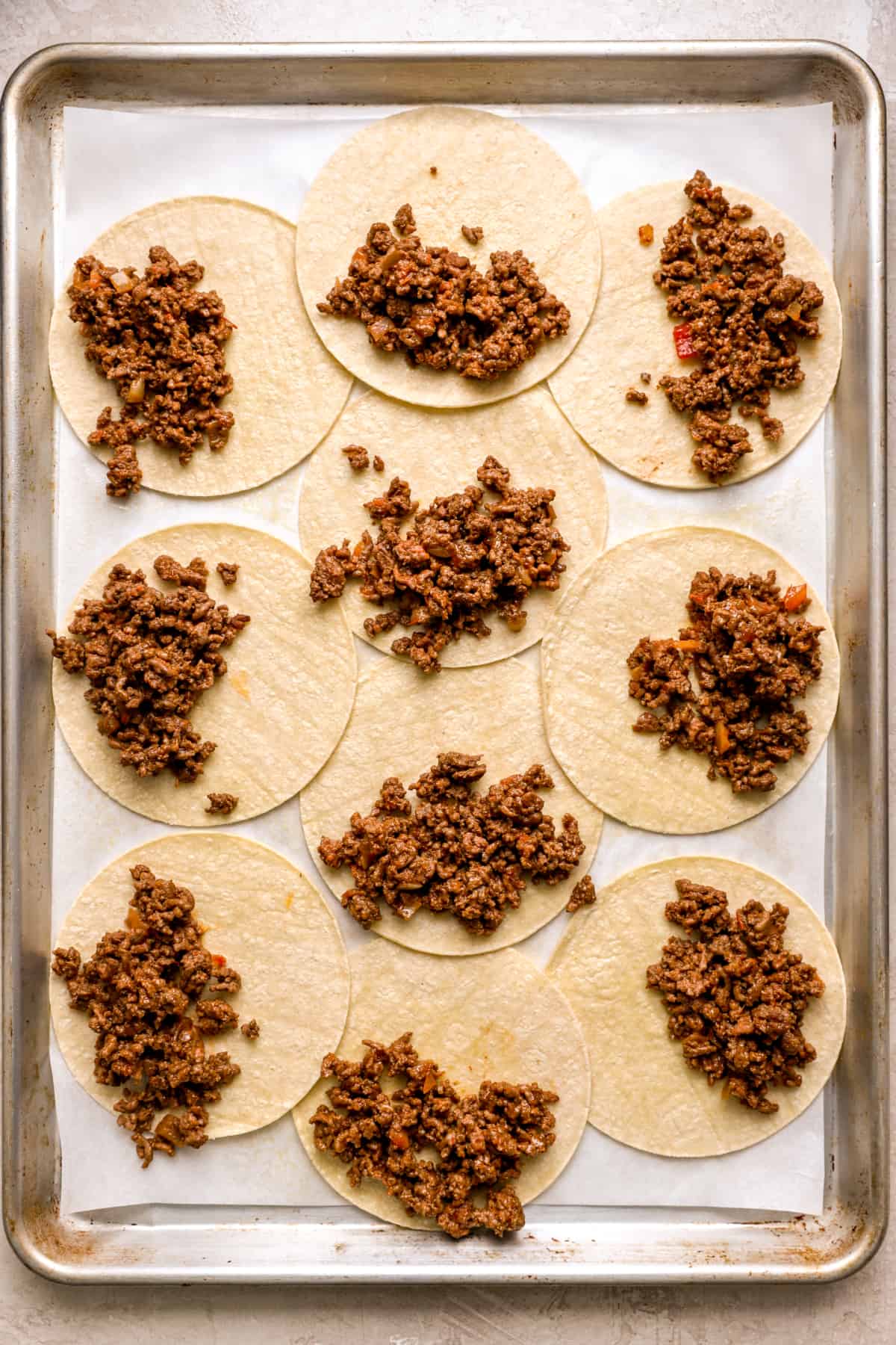 corn tortillas on a baking sheet topped with ground beef.