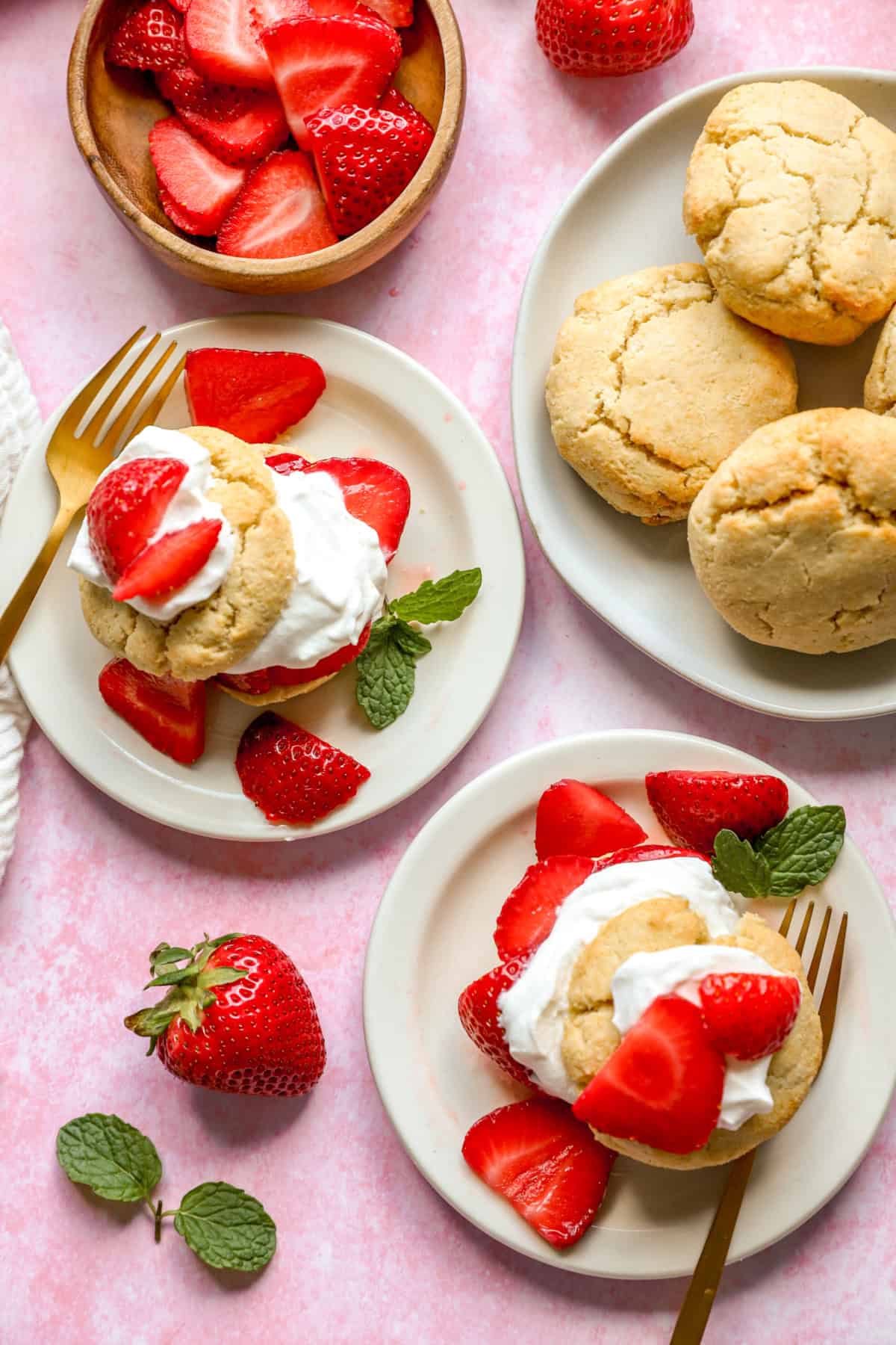Two plates of gluten free strawberry shortcake next to a plate of drop biscuits. 
