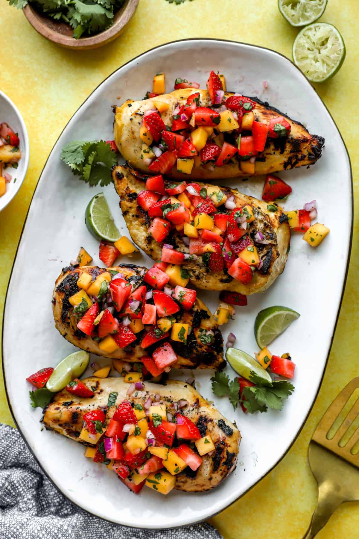A plate of four grilled chicken breasts topped with strawberry mango salsa. 