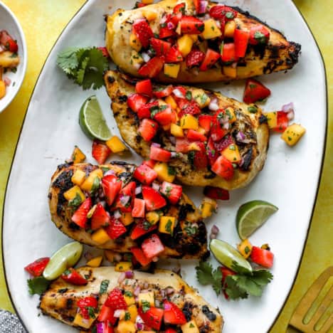 A plate of four grilled chicken breasts topped with strawberry mango salsa.