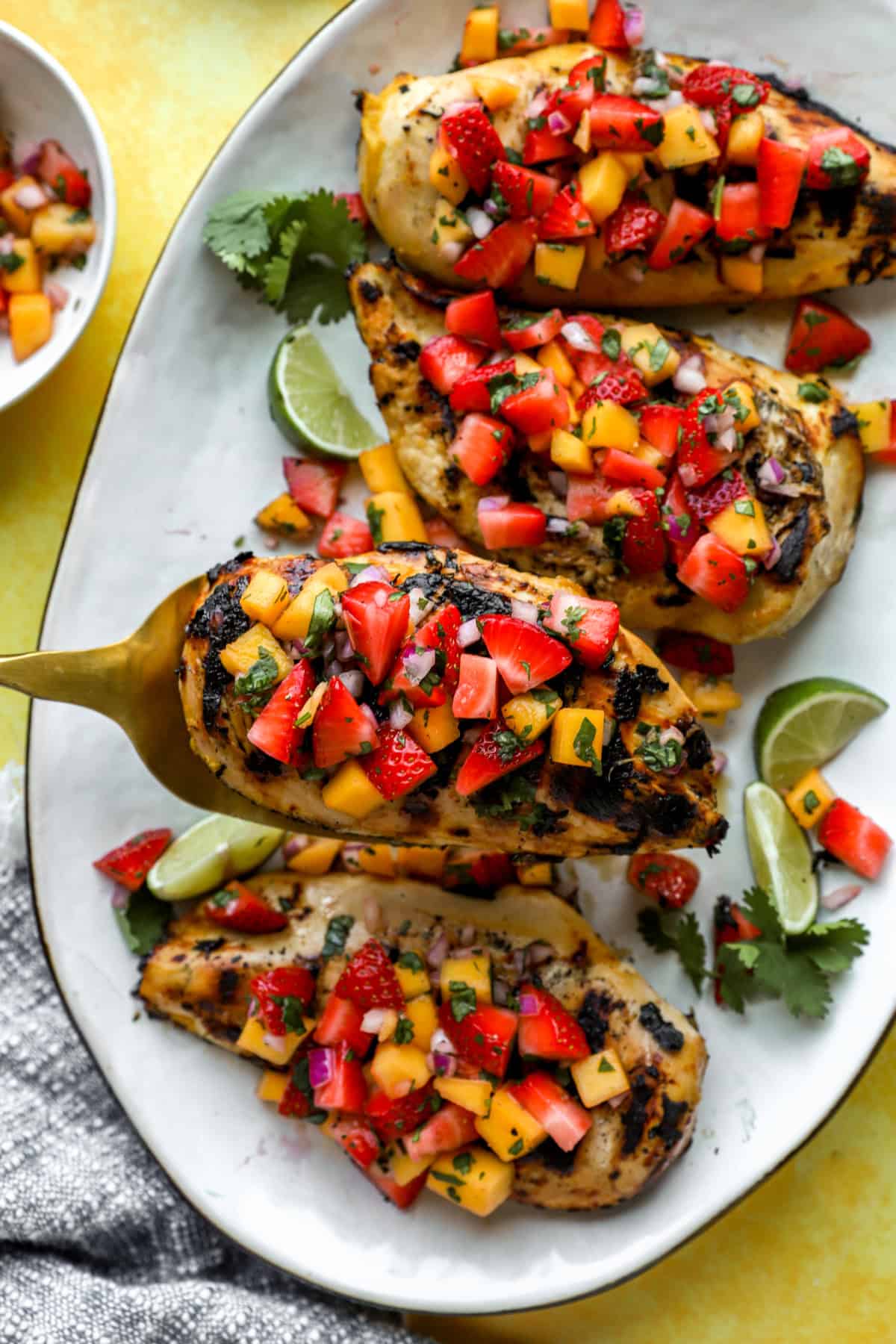 A grilled chicken breast topped with strawberry mango salsa being lifted from a plate. 