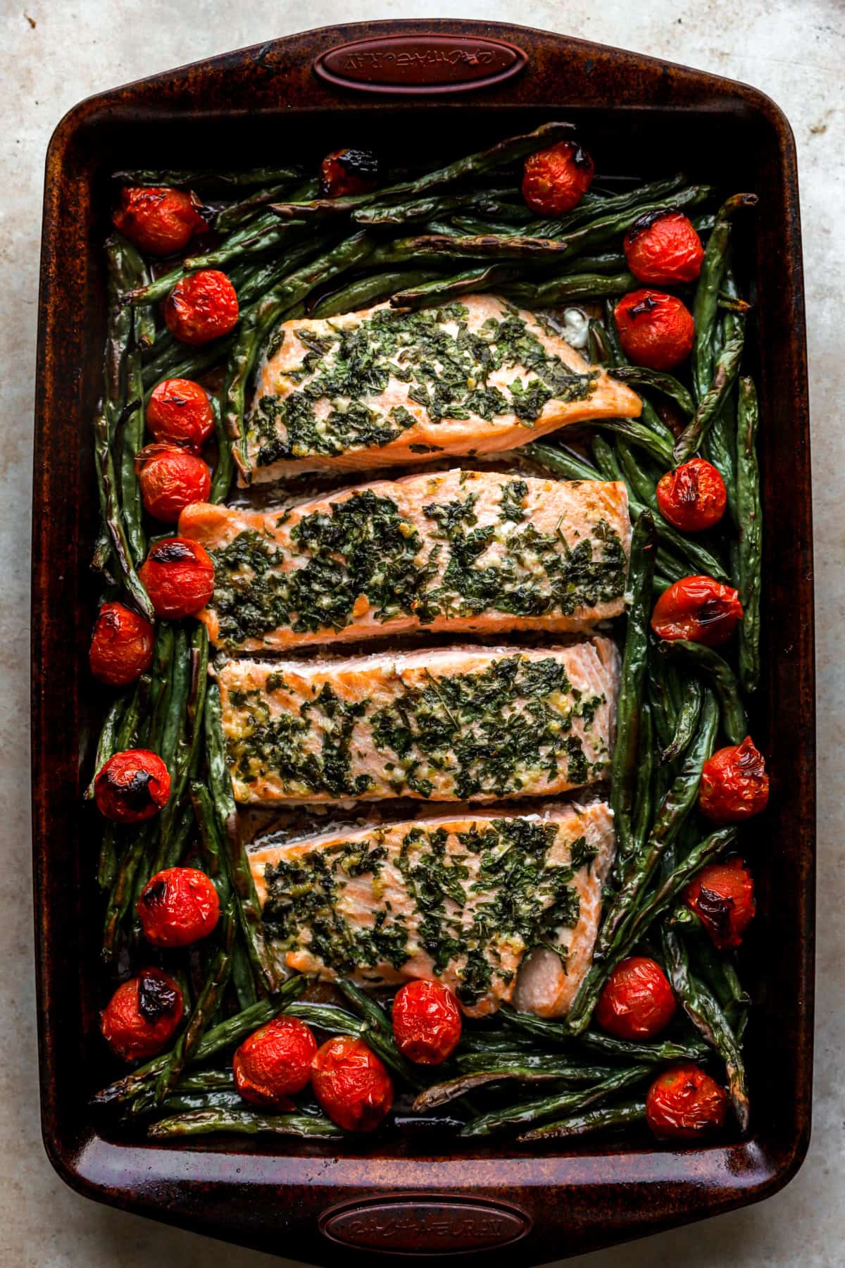 Baked herb butter salmon, green beans, and tomatoes on a baking sheet. 