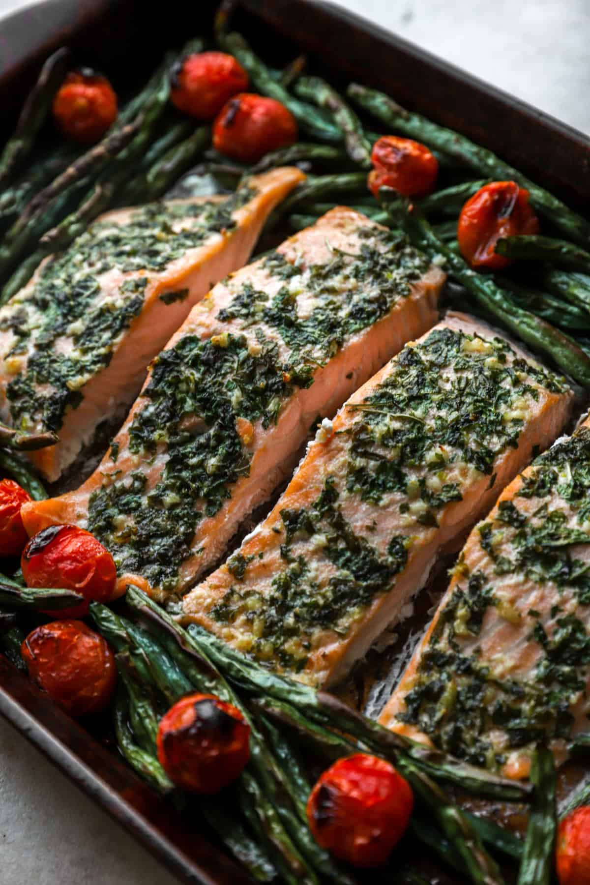 Close up image of herb butter salmon with green beans and tomatoes. 