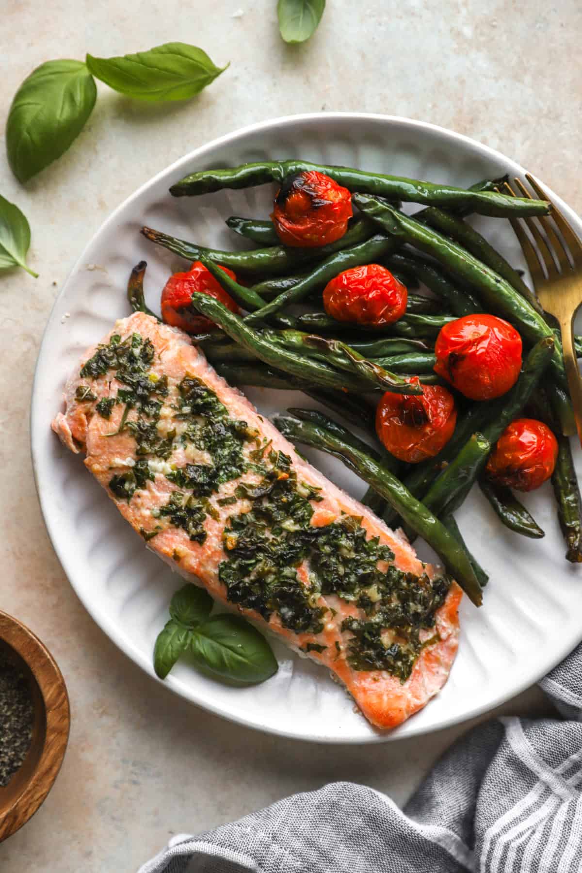 A plate of herb butter salmon with tomatoes and green beans.