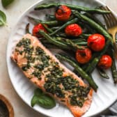 A plate of herb butter salmon with tomatoes and green beans.