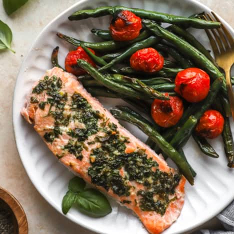 A plate of herb butter salmon with tomatoes and green beans.