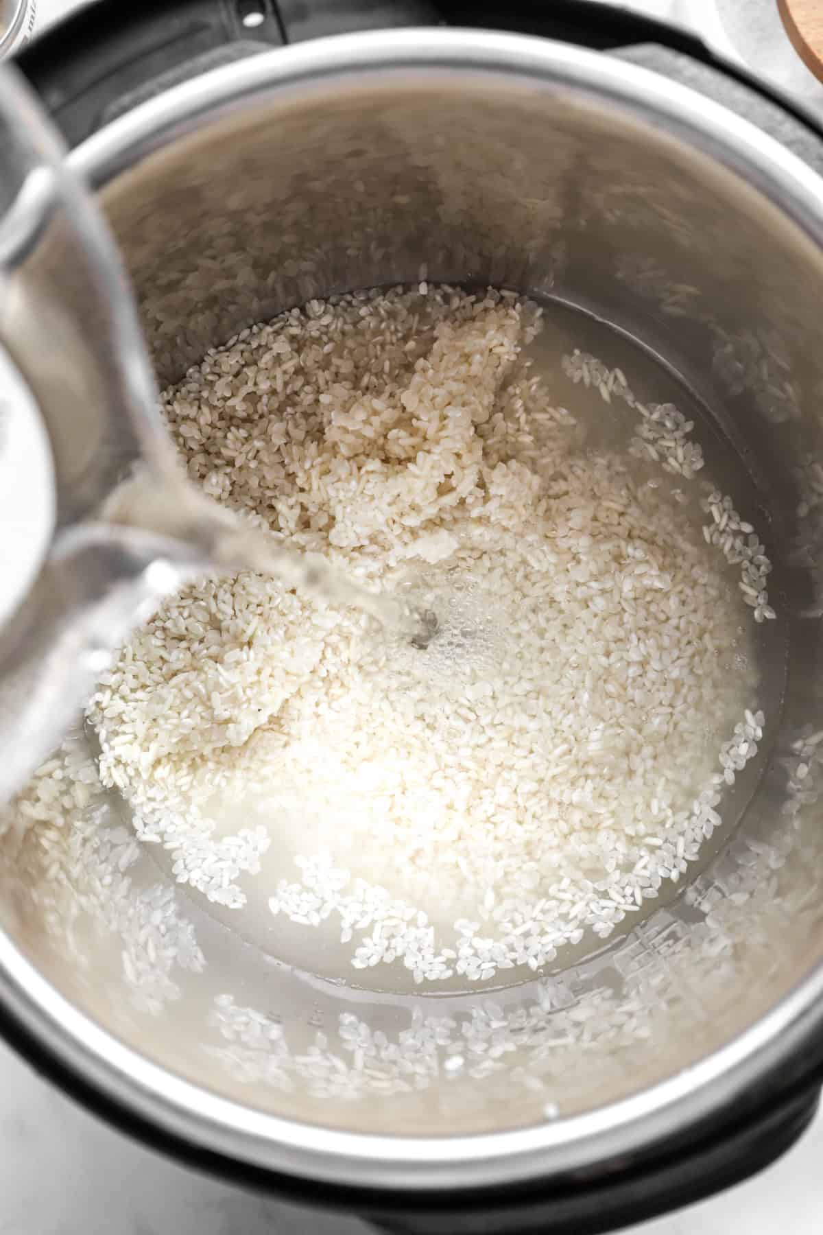 water being poured into the instant pot filled with rice.
