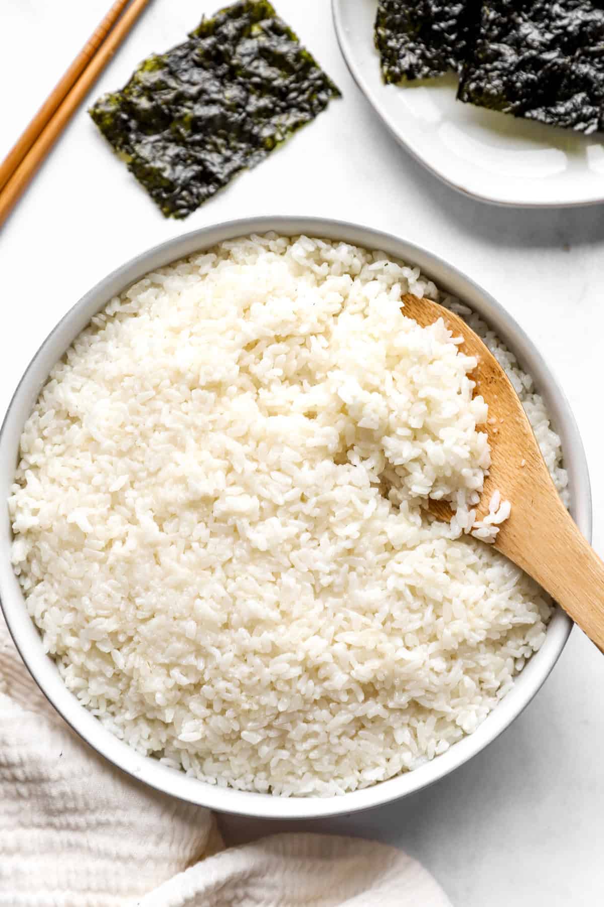 above image of a large bowl full of sticky rice with a wooden spoon and seaweed on the side.
