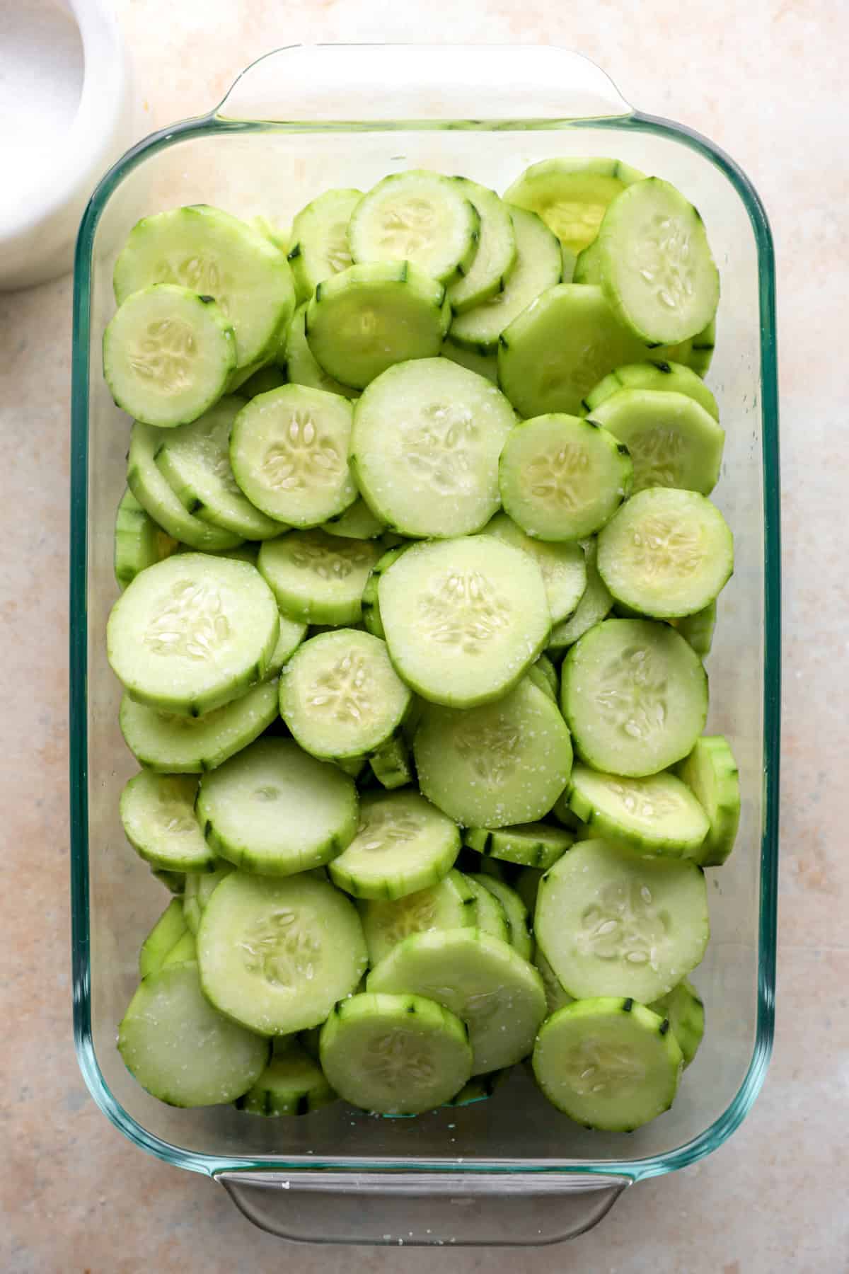 Cucumbers being salted in a glass container. 