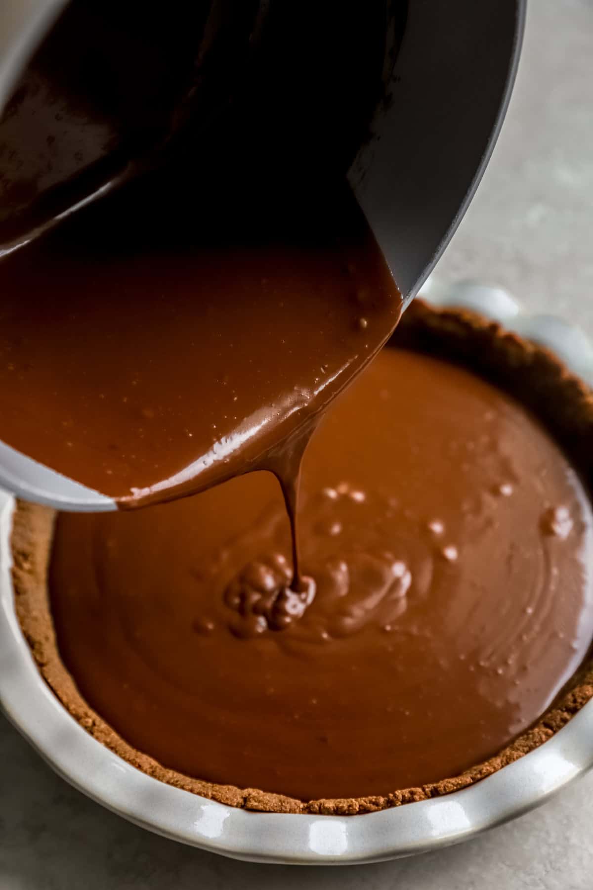 Chocolate filling being poured into a graham cracker crust. 
